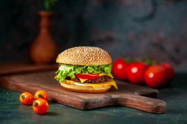 Vista frontal hamburguesa de carne con tomates frescos sobre fondo oscuro