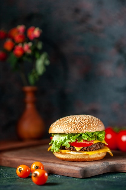 Vista frontal hamburguesa de carne con tomates frescos sobre fondo oscuro