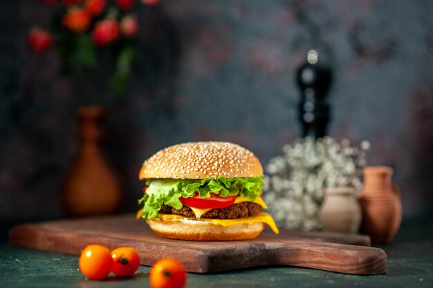 Vista frontal hamburguesa de carne con tomates frescos sobre fondo oscuro