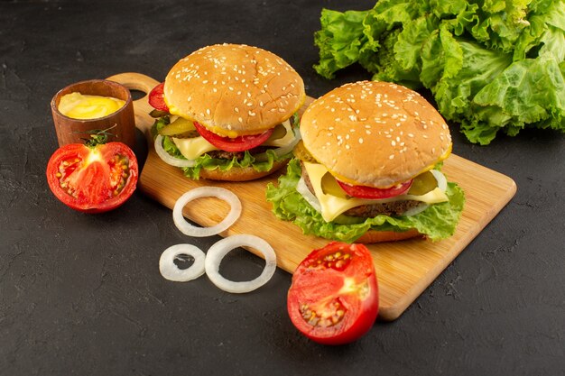 Vista frontal de una hamburguesa de pollo con queso, tomates y ensalada verde en el escritorio de madera y sándwich de comida rápida.