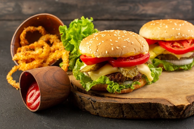 Una vista frontal de hamburguesas de pollo con queso y ensalada verde en el escritorio de madera y sándwich de comida rápida.