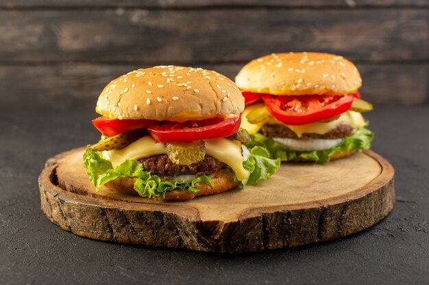 Una vista frontal de hamburguesas de pollo con queso y ensalada verde en el escritorio de madera y sándwich de comida rápida.