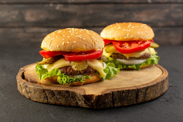 Una vista frontal de hamburguesas de pollo con queso y ensalada verde en el escritorio de madera y sándwich de comida rápida.