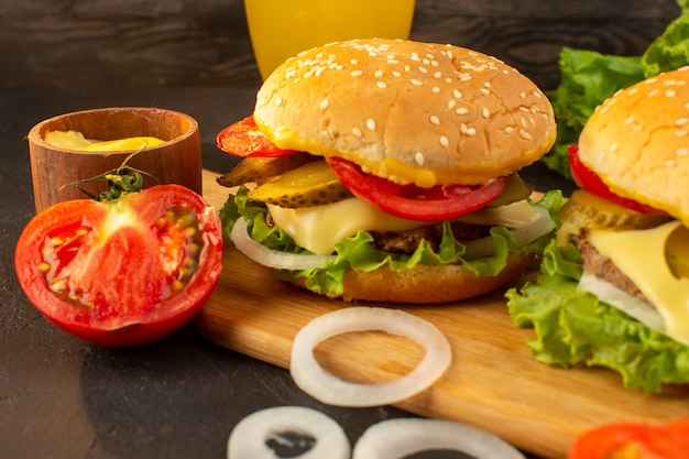 Una vista frontal de hamburguesas de pollo con queso y ensalada verde junto con jugo en el escritorio de madera y sándwich de comida rápida.