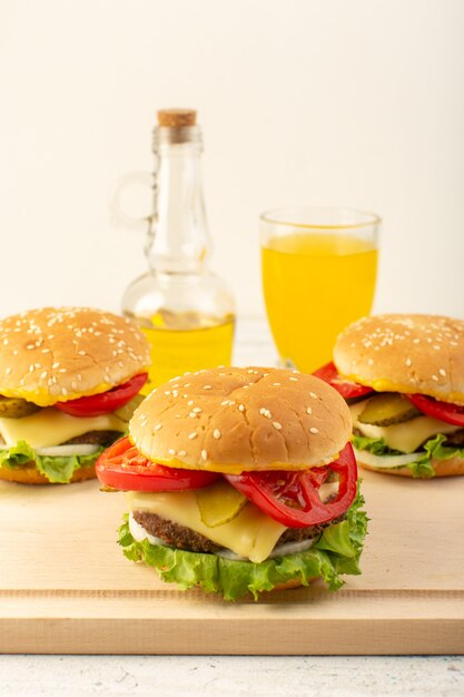 Una vista frontal de las hamburguesas de pollo con queso, jugo de ensalada verde y aceite de oliva en el escritorio de madera y comida rápida sándwich