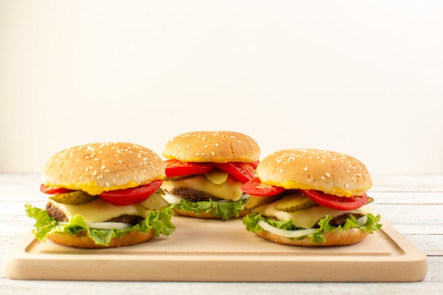 Una vista frontal de hamburguesas de pollo con queso, tomate y ensalada verde en el escritorio de madera y sándwich de comida rápida.