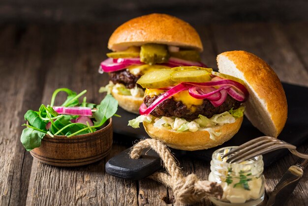 Vista frontal de hamburguesas de ternera con pepinillos y cebollas rojas en la tabla de cortar