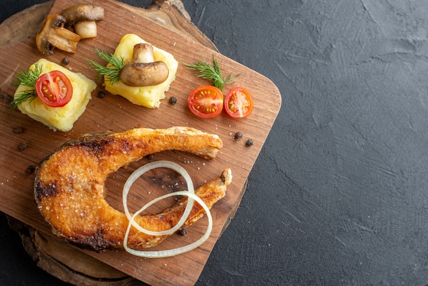 Vista frontal de la harina de pescado frito con champiñones, verduras, queso sobre una tabla de madera en el lado derecho sobre una superficie angustiada negra