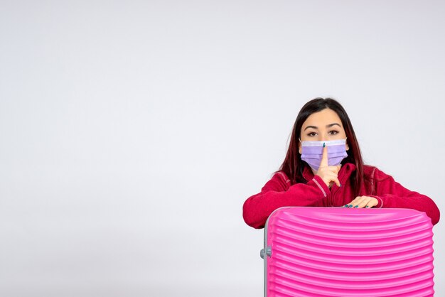 Vista frontal hembra joven con bolsa rosa en máscara estéril sobre pared blanca viaje color covid- mujer pandemia de virus