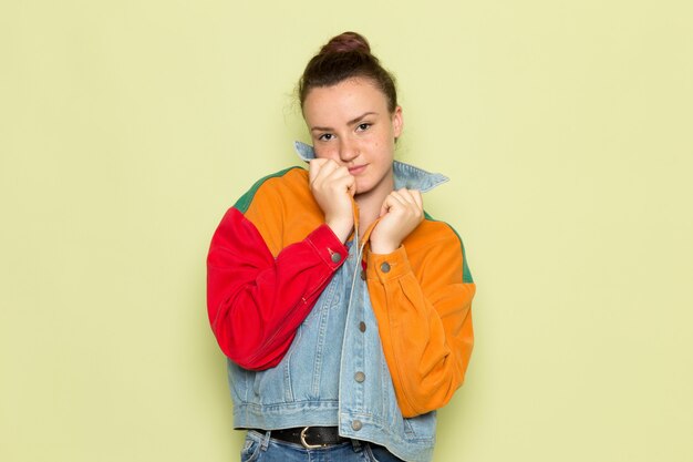 Una vista frontal hembra joven en camisa amarilla chaqueta colorida y jeans azul posando