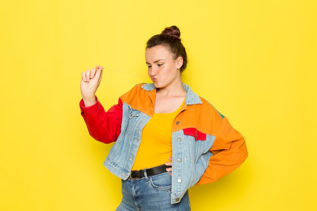 Una vista frontal hembra joven en camisa amarilla chaqueta colorida y jeans azul posando