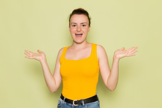 Una vista frontal hembra joven en camisa amarilla y jeans azul con expresión feliz