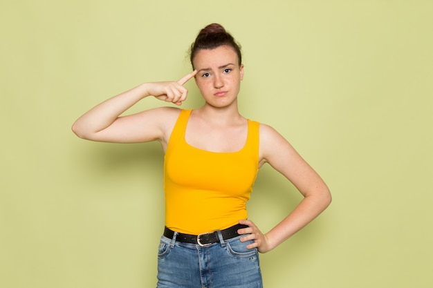 Una vista frontal hembra joven en camisa amarilla y jeans azul con expresión de pensamiento