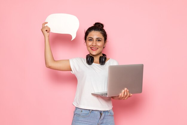 Una vista frontal hembra joven en camiseta blanca y blue jeans con laptop y cartel blanco