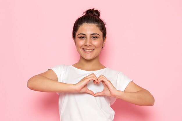 Una vista frontal hembra joven en camiseta blanca y blue jeans posando y mostrando en forma de corazón