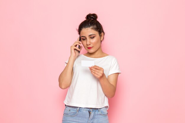 Una vista frontal hembra joven en camiseta blanca y jeans azul hablando por teléfono