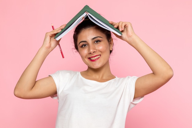 Una vista frontal hembra joven en camiseta blanca y jeans azul sosteniendo un cuaderno con sonrisa