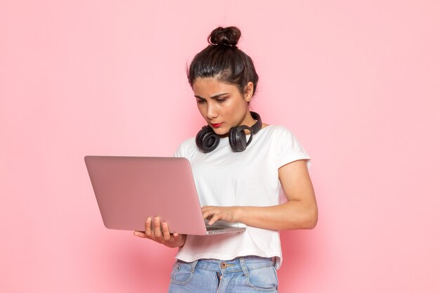 Una vista frontal hembra joven en camiseta blanca y jeans azul usando laptop