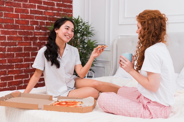 Vista frontal hembra joven en casa comiendo pizza