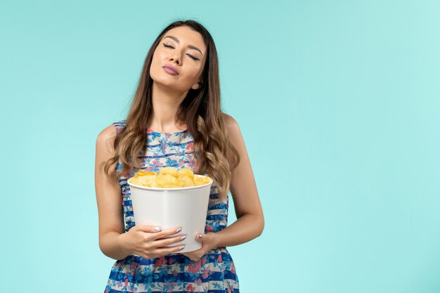 Vista frontal hembra joven sosteniendo la cesta con papas fritas en la superficie azul