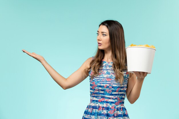 Vista frontal hembra joven sosteniendo la cesta con papas fritas en la superficie azul