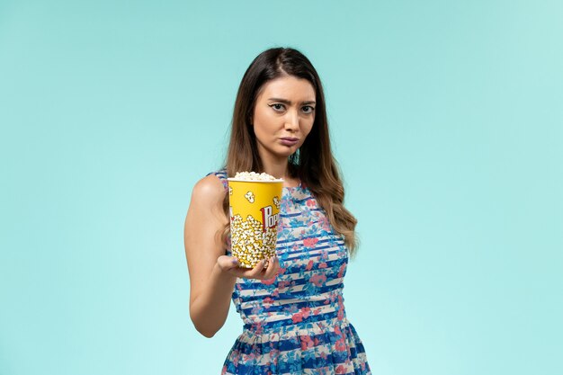 Vista frontal hembra joven sosteniendo el paquete de palomitas de maíz en la superficie azul