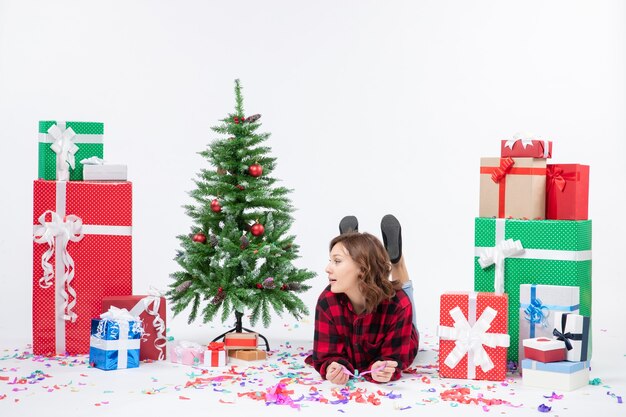 Vista frontal de las hembras jóvenes alrededor de los regalos de Navidad y el árbol de vacaciones tendido sobre fondo blanco Navidad regalo de año nuevo color nieve