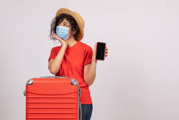 Vista frontal de las hembras jóvenes con bolsa roja en máscara sosteniendo el teléfono sobre un fondo blanco sun covid pandemia de vacaciones viaje turístico virus color