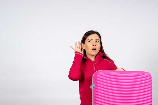 Vista frontal de las hembras jóvenes con bolsa rosa escuchando en la pared blanca emoción vacaciones mujer color viaje viaje vuelo