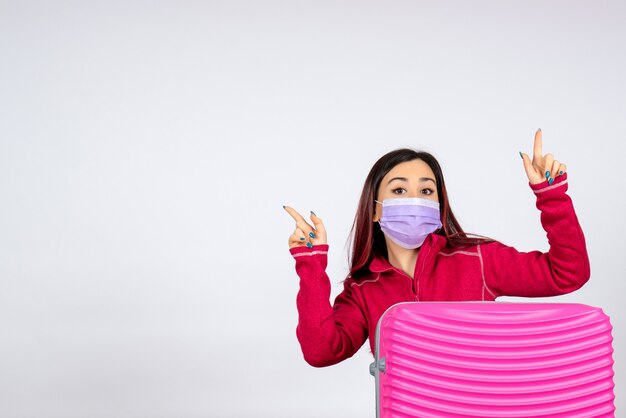 Vista frontal de las hembras jóvenes con bolsa rosa en máscara en la pared blanca mujer virus de la pandemia de vacaciones covid- color