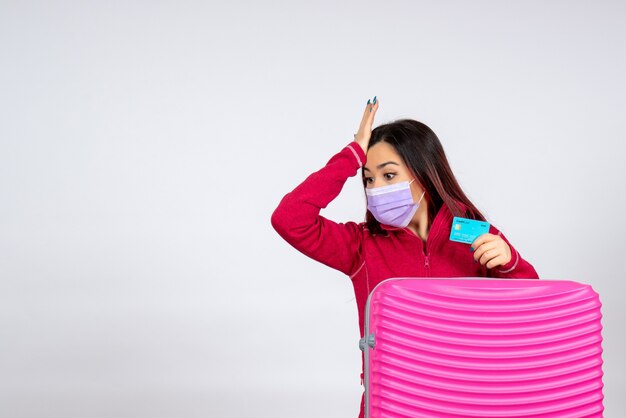 Foto gratuita vista frontal de las hembras jóvenes con bolsa rosa en la máscara que sostiene la tarjeta bancaria en la pared blanca virus mujer vacaciones covid- pandemia de viaje de color