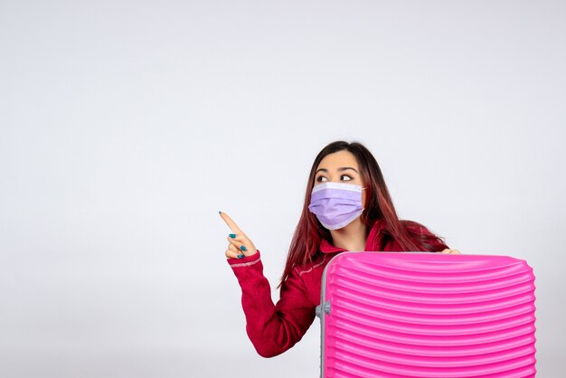Vista frontal de las hembras jóvenes con bolsa rosa en máscara sosteniendo el mapa en la pared blanca color virus mujer pandemia de vacaciones covid-