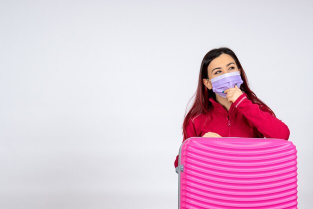 Foto gratuita vista frontal de las hembras jóvenes con bolsa rosa en la máscara sosteniendo el mapa en la pared blanca pandemia de vacaciones de virus mujer viaje covid-