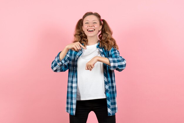 Vista frontal de las hembras jóvenes en camisa a cuadros azul apuntando su muñeca en la pared rosa niño joven emoción modelo mujer color