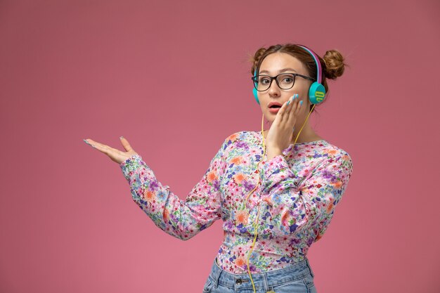 Vista frontal de las hembras jóvenes en camisa de diseño floral y jeans con auriculares escuchando música en el fondo rosa