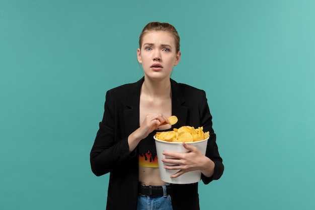 Vista frontal de las hembras jóvenes comiendo patatas fritas viendo la película en la superficie azul claro