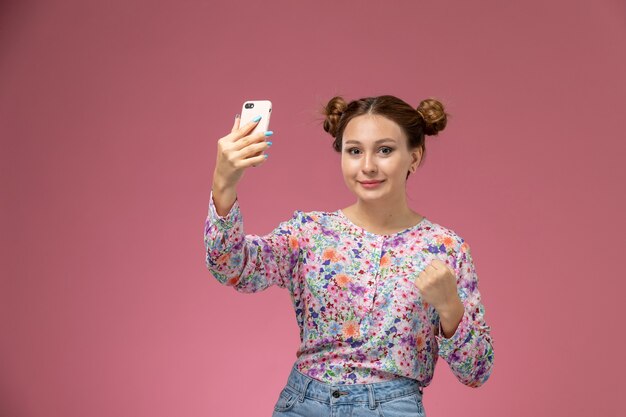 Vista frontal de las hembras jóvenes en flor diseñada camisa y jeans tomando un selfie con una sonrisa sobre fondo rosa