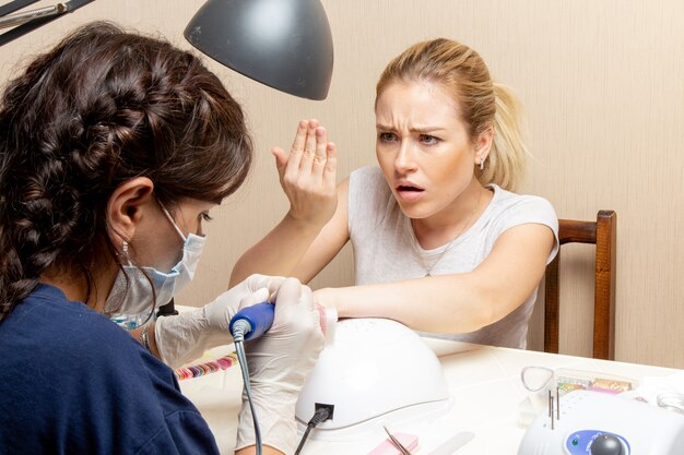 Vista frontal de las hembras jóvenes obteniendo sus uñas arregladas por manicurista dentro de la habitación belleza mujer manicura uñas autocuidado dama