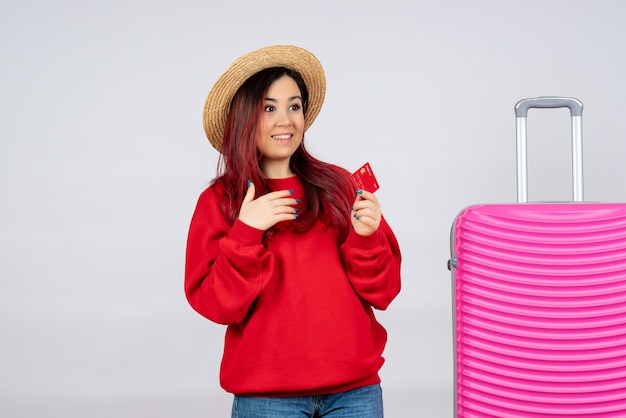 Vista frontal de las hembras jóvenes preparándose para el viaje y sosteniendo la tarjeta bancaria en la pared blanca vacaciones color vuelos verano emoción viaje