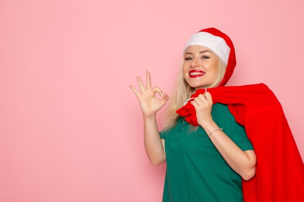 Vista frontal de las hembras jóvenes que llevan bolsa roja con regalos en la pared rosa modelo vacaciones navidad año nuevo color foto santa