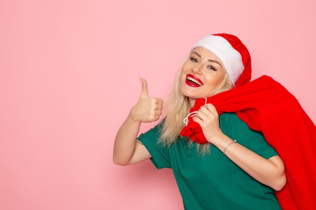 Vista frontal de las hembras jóvenes que llevan bolsa roja con regalos en la pared rosa modelo vacaciones navidad año nuevo color foto santa