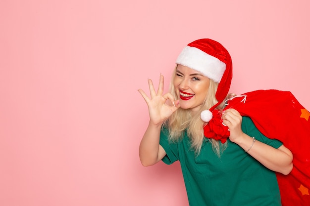 Vista frontal de las hembras jóvenes que llevan bolsa roja con regalos en la pared rosa modelo de vacaciones Navidad año nuevo foto en color santa