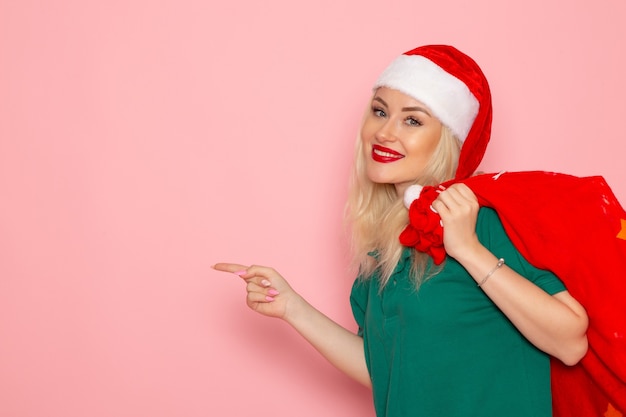 Vista frontal de las hembras jóvenes que llevan una bolsa roja con regalos en la pared rosa modelo de vacaciones navidad año nuevo foto santa