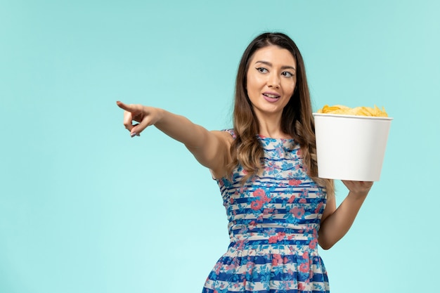 Vista frontal de las hembras jóvenes que sostienen la canasta con papas fritas en la superficie azul claro