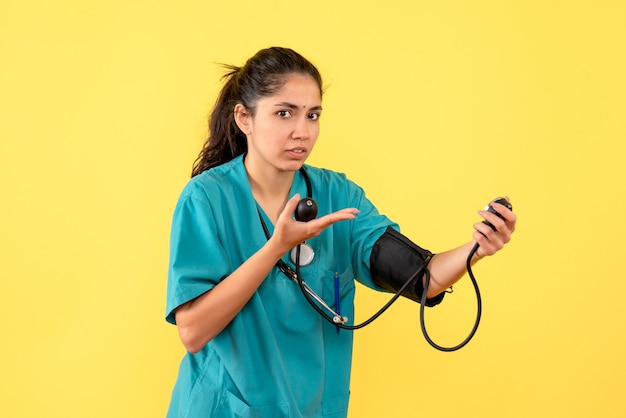 Vista frontal hermosa doctora en uniforme sosteniendo esfigmomanómetros sobre fondo amarillo