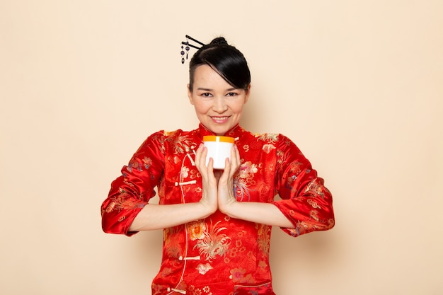 Foto gratuita una vista frontal hermosa geisha japonesa en el tradicional vestido rojo japonés con palos de pelo posando sonriendo feliz celebración crema puede en la ceremonia de fondo crema japón