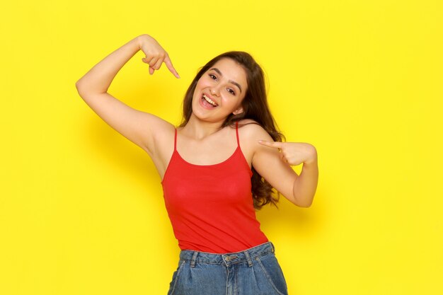 Una vista frontal hermosa joven en camisa roja y jeans azul posando con expresión emocionada