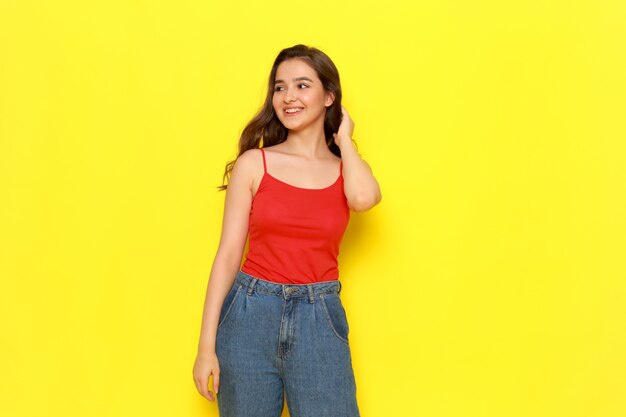 Una vista frontal hermosa joven en camisa roja y pantalones vaqueros azules de pie con una sonrisa