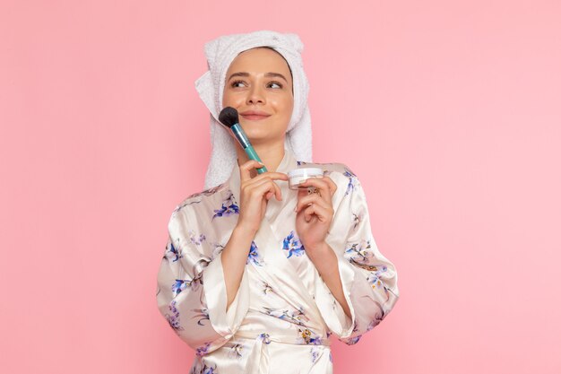 Una vista frontal hermosa jovencita en bata de baño haciendo maquillaje con sonrisa