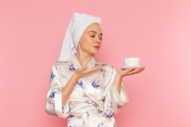 Una vista frontal hermosa jovencita en bata de baño con taza de café